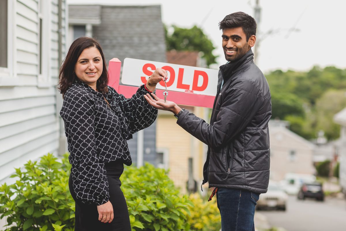 Agent handing keys to a buyer in front of a sold property